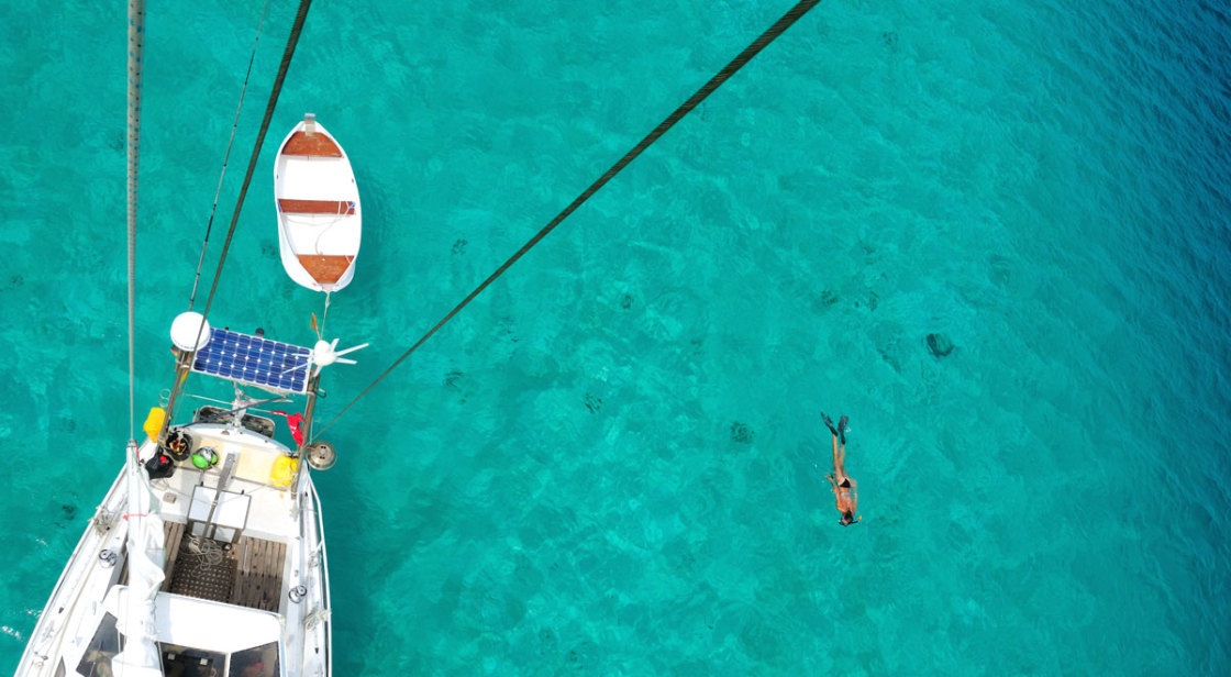 Inspiration with woman swimming in crystal clear water next to sailboat