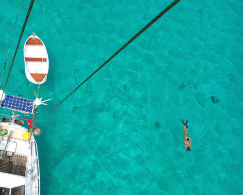 snorkling next to Karl Inspiration with woman swimming in crystal clear water next to sailboat