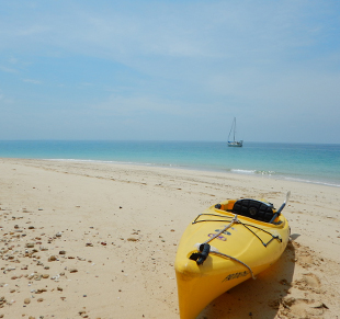 Kayak on white beach in Belize with a sailboat